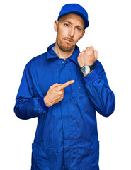Bald man with beard wearing builder jumpsuit uniform in hurry pointing to watch time, impatience,...