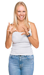 Young blonde girl wearing casual style with sleeveless shirt smiling funny doing claw gesture as...