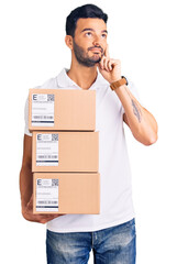 Young handsome hispanic man holding delivery package serious face thinking about question with hand...