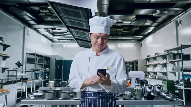 Asian Man Chef Smiling And Using Smartphone While Standing In Kitchen