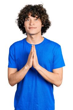 Caucasian teenager wearing casual clothes praying with hands together asking for forgiveness smiling confident.