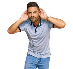 Fototapeta premium Handsome man with beard wearing casual clothes trying to hear both hands on ear gesture, curious for gossip. hearing problem, deaf