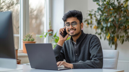 Smiling man on the phone while using a laptop.