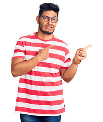 Handsome latin american young man wearing casual clothes and glasses pointing aside worried and...