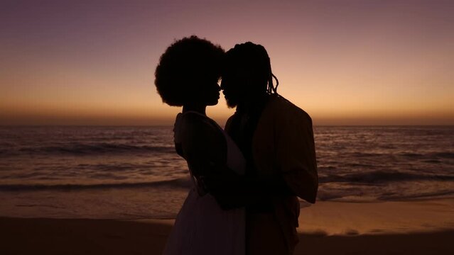 Silhouette of an African couple sharing a romantic embrace at the beach against a stunning sunset backdrop, portraying love and intimacy.