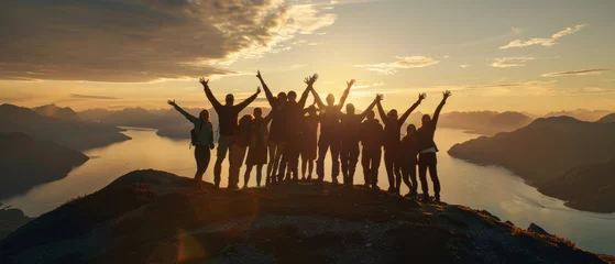 Foto op Aluminium On a mountaintop, a large group of people are enjoying a success pose with their arms raised against a sunset lake and mountains. This is a concept for travel, adventure, or expedition. © Zaleman