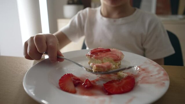 Small boy eating strawberry cheesecake on plate closeup. One 5 year old child takes a bite of sweet dessert after mealtime