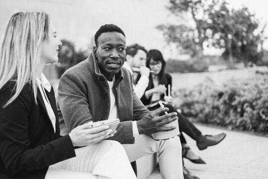 Multiracial colleagues eating together outdoor at city park during luch break - Diversity and job concept - Black and white editing - Focus on african man face