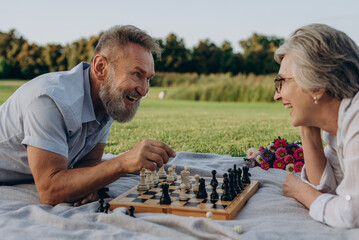 Loving married couple playing chess in public park - 767884773