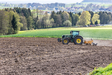 A tractor cultivates a plowed field in the spring