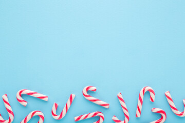 Red white candy canes on light blue table background. Pastel color. Closeup. Sweet food. Empty place for text. Top down view.