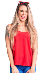 Fototapeta premium Young beautiful blonde woman wearing sleeveless t-shirt and sunglasses winking looking at the camera with sexy expression, cheerful and happy face.