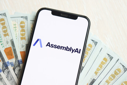 KYIV, UKRAINE - MARCH 17, 2024 AssemblyAI logo on iPhone display screen with many hundred dollar bills. Artificial Intelligence engine