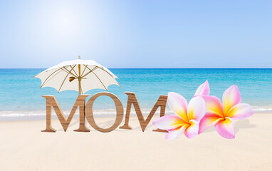 Mother's day card background idea, Mom wooden text with plumeria flower and white umbrella on tropical beach, outdoor day light