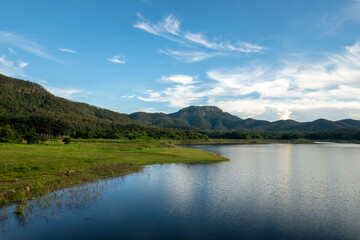 Fototapeta na wymiar Serene Lake with Lush Hills Under a Blue Sky