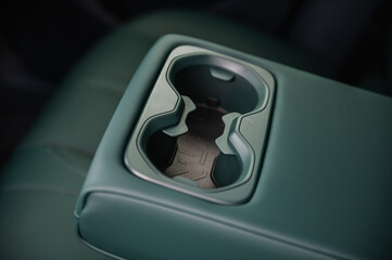 Car cup holders between back seats, closeup view. Part of green leather car seat. Luxury car...