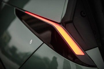 The left rear light shining on a new modern electric sedan car. Red tail lights closeup. Modern...