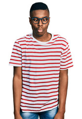 Young african american man wearing casual t shirt and glasses making fish face with lips, crazy and comical gesture. funny expression.