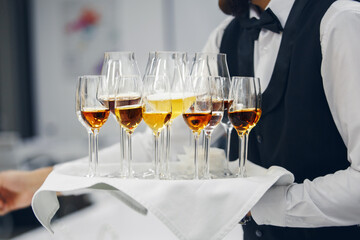 Various alcoholic beverages in different glass on tray holding wine waiter, close up. Service, serving concept.