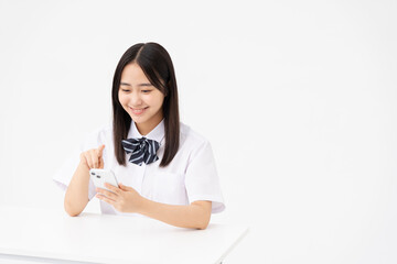 Naklejka premium 制服を着た日本人女子高校生/スマートフォンの画面を見ている/白背景スタジオ撮影 