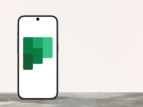 Microsoft Planner logo is displayed on a modern smartphone standing on a desk, planning application available on the Microsoft 365 platform, team management, file sharing, and organization