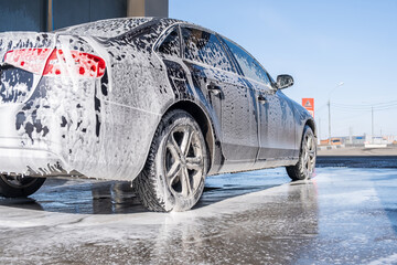 A vehicle is engulfed in soapy foam during a car wash, covering the tires, wheels, hood, and entire...