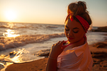 Portrait os A beautiful plus size woman dressed solid  pink swimsuit, jeans shorts, sunglasses and...