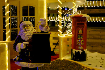 Festive Santa Claus figure standing illuminated by glowing Christmas lights, holding a box