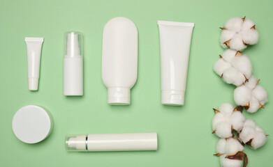 White plastic tubes, jars, and containers for cosmetic products on a green background