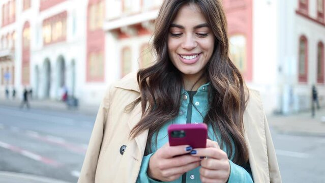 Happy Latin woman using smartphone in the city