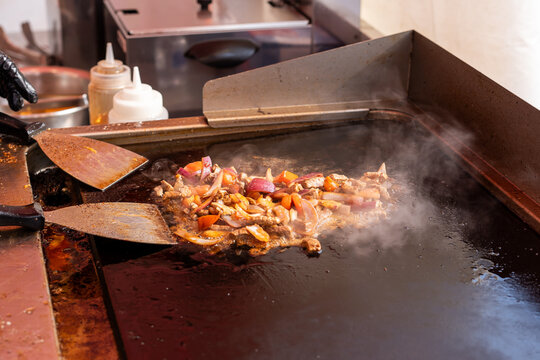 cooking vegetables and pieces of meat on the griddle of the stall. Street food