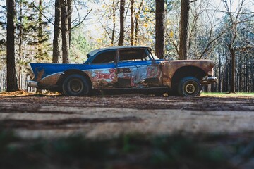 Closeup of a  vintage blue car parked on a forest path, surrounded by tall trees © Wirestock