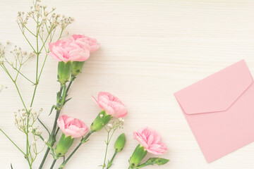 Pink carnations, white hazel, and pretty pink envelopes on a white wooden table.	