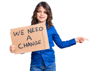 Cute hispanic child with long hair holding we need a change banner smiling happy pointing with hand and finger to the side