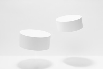 Abstract white scene mockup - two round tilt white cylinder podiums levitate in hard light, shadow....
