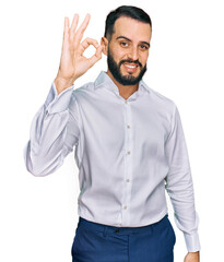 Fototapeta premium Young man with beard wearing business shirt smiling positive doing ok sign with hand and fingers. successful expression.