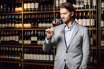 Sommelier smelling flavor of red wine in glass on background of shelves with bottles in cellar.
