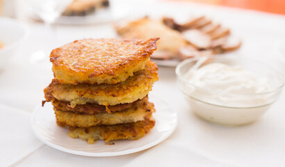 Fried grated potato pancakes with sour cream on white plate