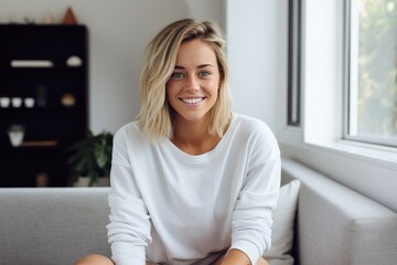 Obraz premium Attractive blonde woman sitting in a modern home wearing casual clothing and smiling, happy mood, happy life