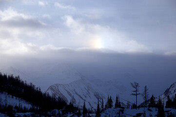 Sunlight breaks through clouds above snowcovered mountains.