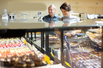 Female customer chooses sweet cakes with interest of the grocery department of supermarket