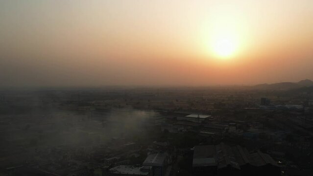Drone footage over smoky sky over cityscape with orange sunset sky on the horizon