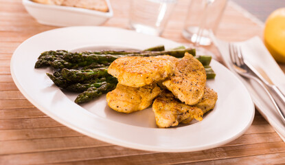 Fried chicken breast pieces with asparagus on white plate