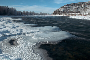 A frozen river bank with a distant mountain under a cloudy sky