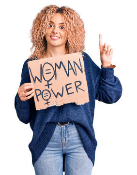 Young blonde woman with curly hair holding we need a change banner surprised with an idea or question pointing finger with happy face, number one