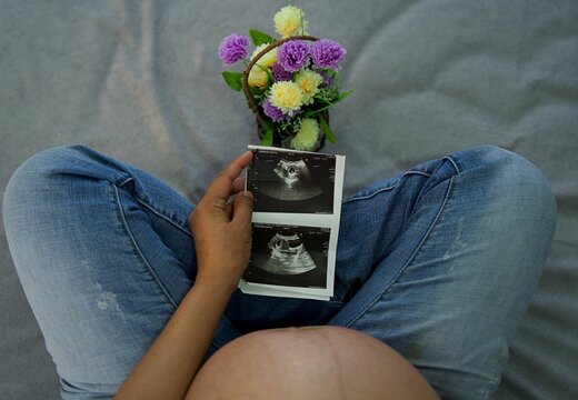 Pregnant mother in jeans holding the ultrasound pictures near a vase of flowers