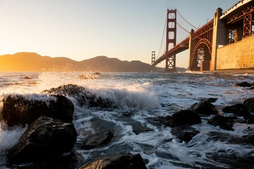 Rolling waves crashing onto the shoreline with Golden Gate Bridge in the background at sunset