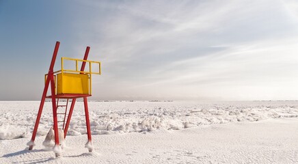 Wooden lifeguard tower stands near the black sea covered in snow in winter