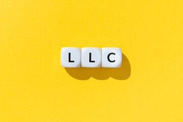 LLC or Limited Liability Company text on white cube blocks isolated on yellow background