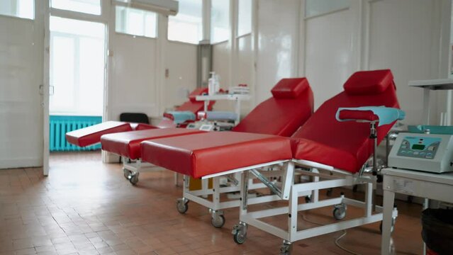 Red medical couches and chairs stand in the large empty room of the blood transfusion center. Medicines and test tubes on the table close-up. Vaccination during an epidemic, medicine and healthcare